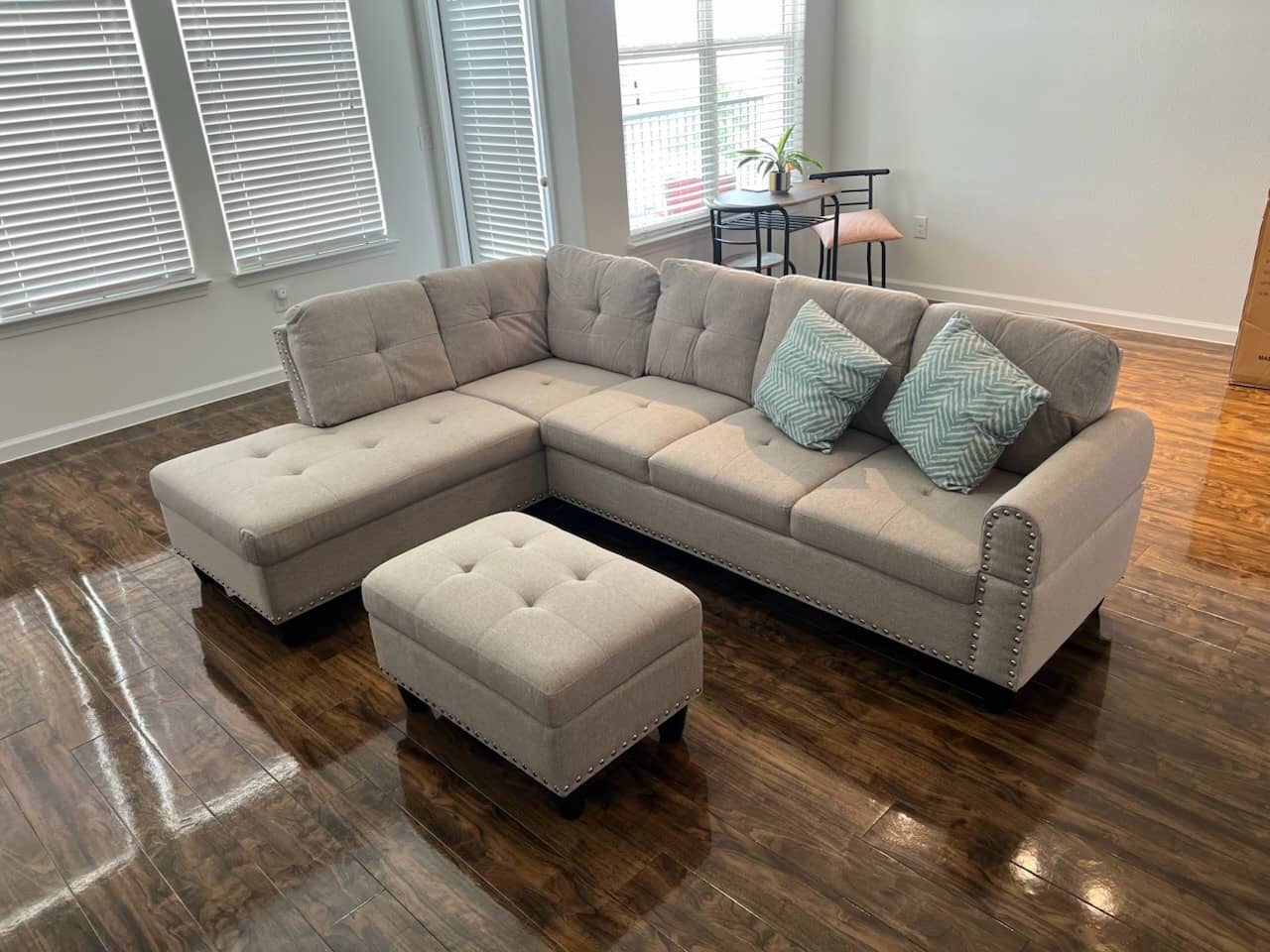 Gray tufted sectional sofa with ottoman assembled in a living room with hardwood floors