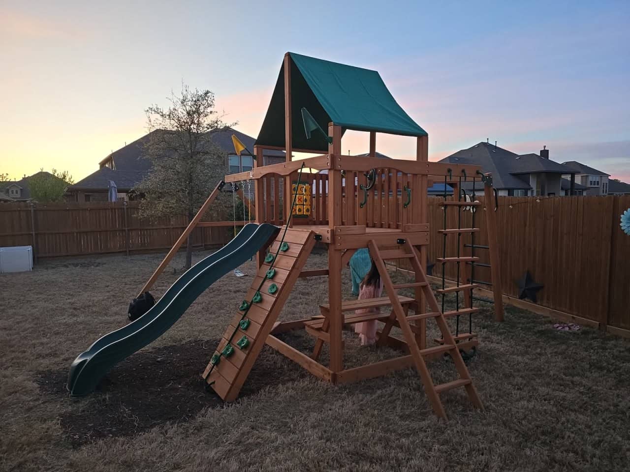 Large wooden playset with slides, swings, and climbing wall assembled in a backyard